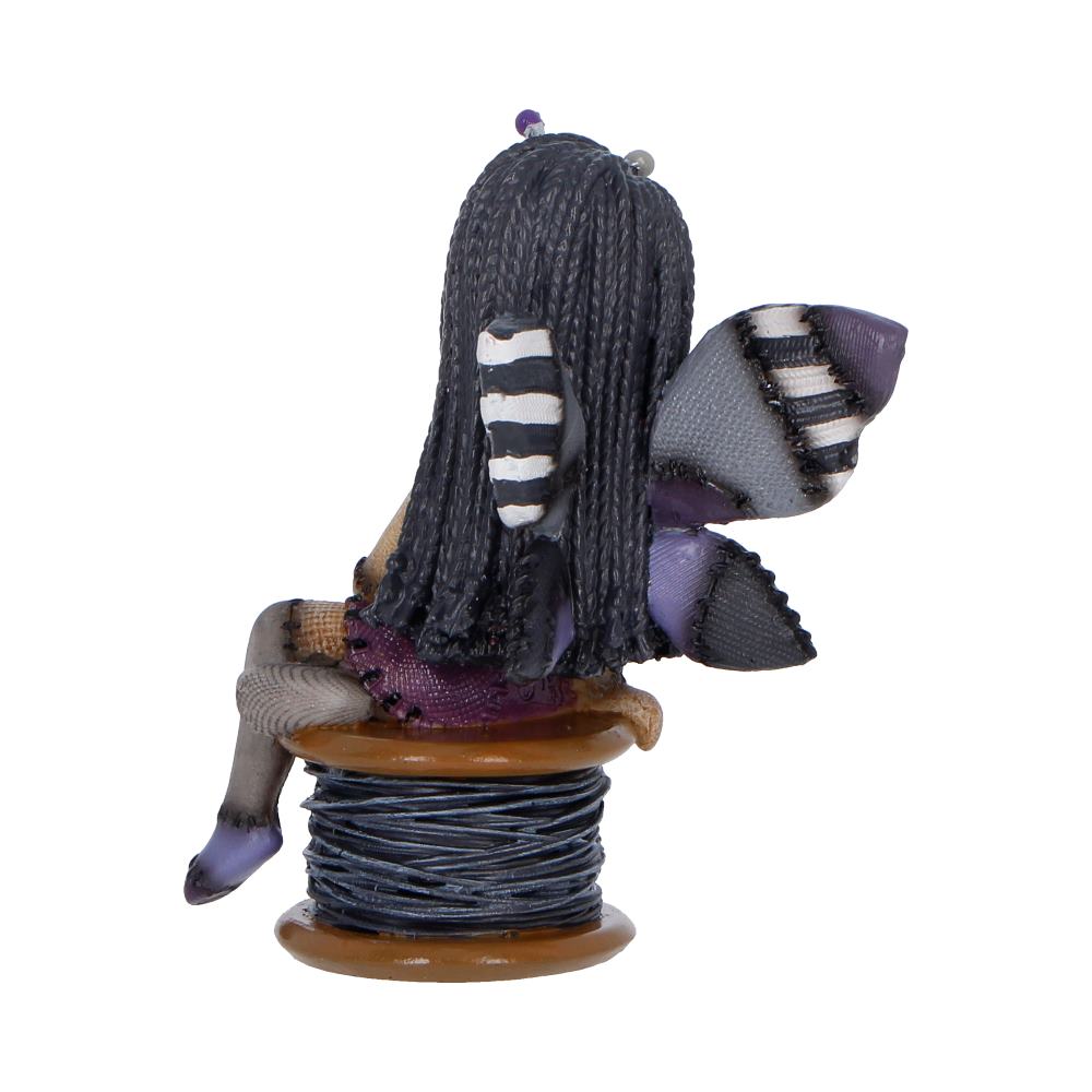 Back view of a small handmade fabric doll with braided hair sitting on a spool of blue thread