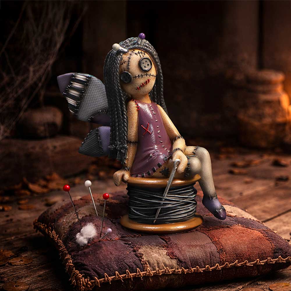 Handmade stitched doll with button eyes and patchwork dress sits on a spool of thread atop a quilted cushion, pins nearby.