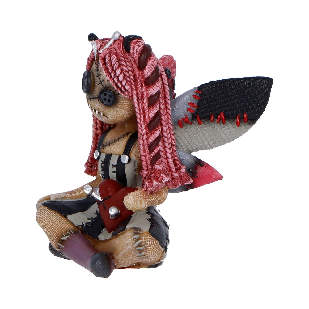Stitched teddy bear figurine with red yarn hair, patchwork clothing, wings, and a red heart in its lap.