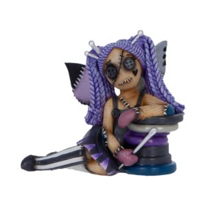 Handmade plush figure of a stitched Frankenstein-like girl with purple yarn hair and button eyes, seated beside a stack of sewing spools and pins.