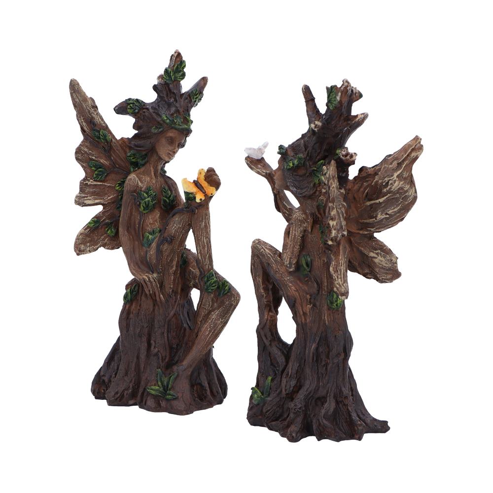 Two fairy statues carved from tree trunks with wings and green leaf accents, posed as woodland figures with a small flower nearby.