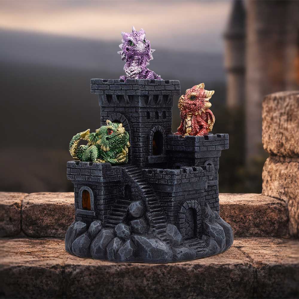Miniature dark stone castle with three colorful dragon figurines perched on top, on a stone surface.